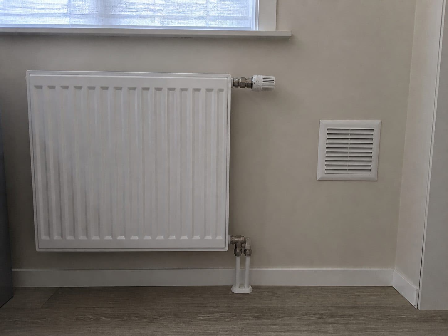 Radiator en ventilatierooster netjes afgewerkt in een woning.